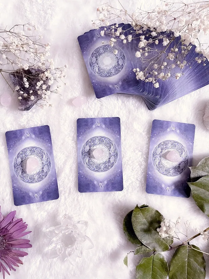 Three violet tarot card backs laid on soft white fur with gypsophila, green leaves and a clear crystal