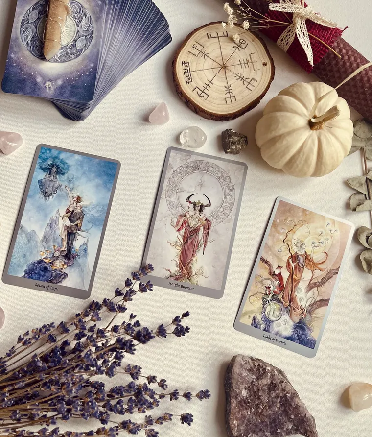Tarot cards laid on a white cloth beside lavender, an amethyst and a wooden disc